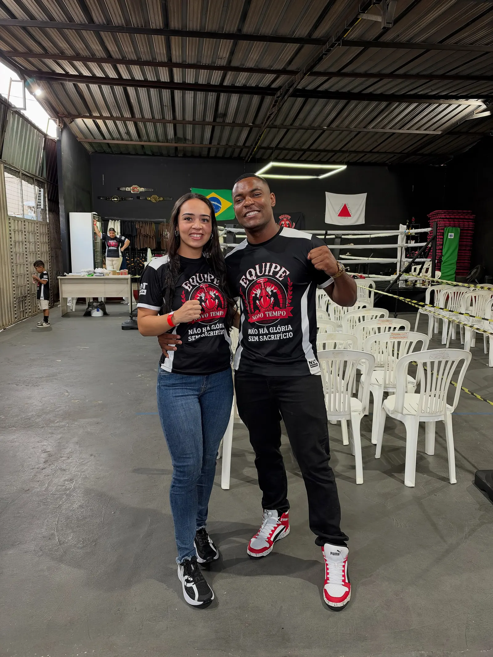 João do Boxe e a esposa, Andressa, de punho erguido e com a camisa da Equipe Novo Tempo, no galpão de treino